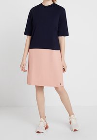 Námořnická modrá blůza s krátkým rukávem, přecházející do jemné růžové sukně. Hladký materiál a pohodlný střih, doplněné světle barevnými sportovními botami.