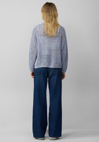Hellblauer, gestrickter Pullover mit offener Maschenstruktur, kombiniert mit lockeren, dunkelblauen Denimhosen. Das Outfit hat eine entspannte, lässige Passform.