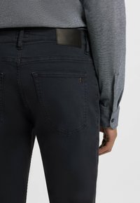 Los jeans de mezclilla azul oscuro cuentan con un ajuste ceñido, bolsillos traseros con costuras sutiles y una etiqueta de cuero negro en la cintura.