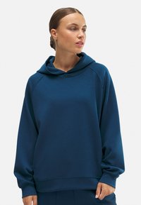 Sudadera azul con capucha que presenta un corte relajado, mangas raglán y una textura suave. La tela es lisa, con costuras y detalles mínimos.