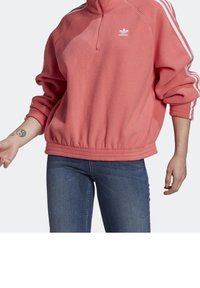 Korallfleecepolo med halvdragkedja, ribbad nederdel och vita tre-rands accenter på ärmarna. Vit logotyp på bröstet.