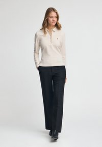 Beżowe polo z długim rękawem, z zapięciem na guziki i logo, połączone z czarnymi spodniami o prostych nogawkach oraz botkami za kostkę.