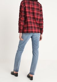 Rood en zwart geblokt shirt met gestructureerde mouwen, gecombineerd met lichtblauwe rechte jeans en zwarte blokhak schoenen.