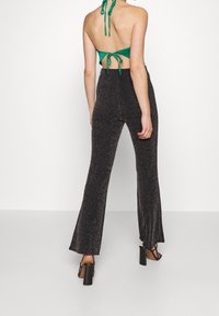 Pantalon évasé noir et scintillant associé à un haut dos nu vert. Le pantalon présente une finition texturée et brillante, tandis que le haut arbore un design noué dans le dos.