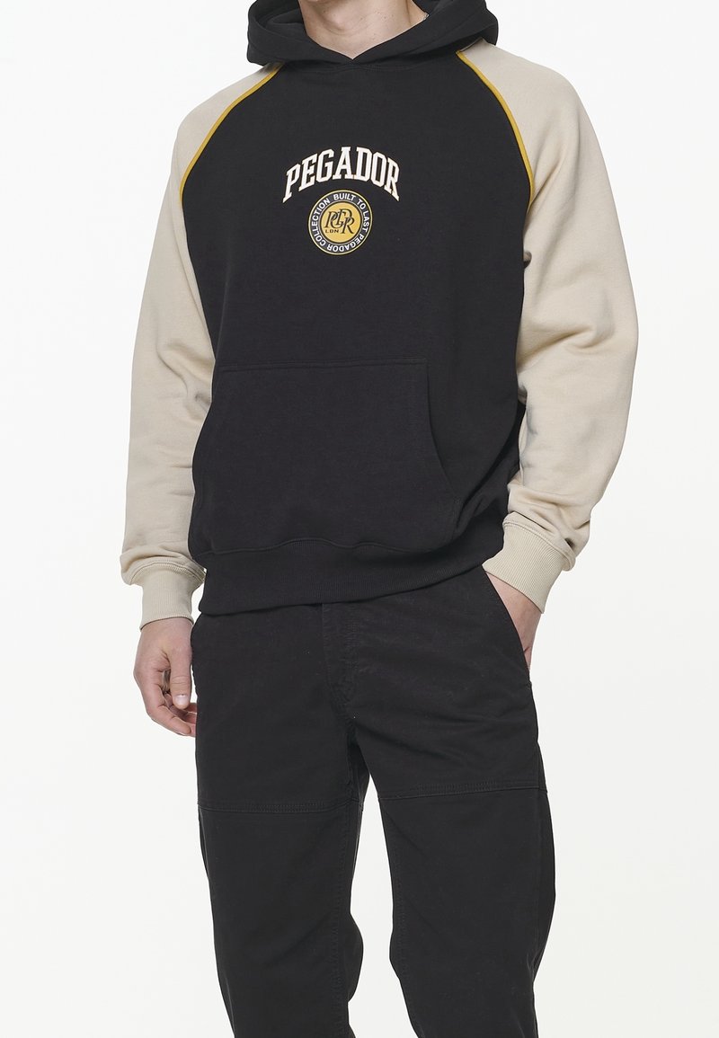 Hoodie noir et beige avec une poche kangourou, un capuchon à cordon coulissant et un logo rond sur la poitrine. Présente un design de manches contrastées.
