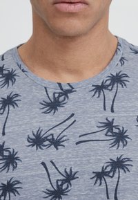 Tričko s krátkým rukávem a kulatým výstřihem světle modré barvy s tmavě modrým potiskem palmy. Vyrobeno z měkkého textilu s hladkou strukturou.