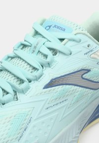 Shoe atlética azul claro com parte superior em malha para respirabilidade, detalhes texturizados, sola padrão e atacadores. Apresenta logo e detalhes de ventilação.