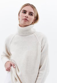 Sweter w kolorze kremowym z golfem i ściągaczami. Miękka tekstura, luźny krój oraz subtelne różnice w materiale.