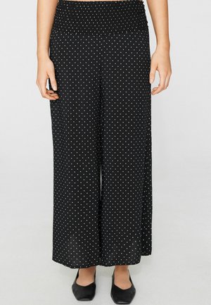 Schwarze weit geschnittene Hosen mit weißen Polka-Dots, hoher geraffter Taille, getragen mit schwarzen spitzen flachen Schuhen.