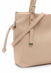 Beige leather handbag with a structured shape, adjustable strap, gold hardware, and a textured finish. Features a decorative knotted detail.