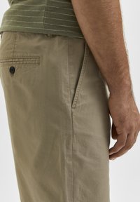 Beiga bomullschinos med en mjuk textur, med en sidficka och en enda bakficka med en svart knapp.