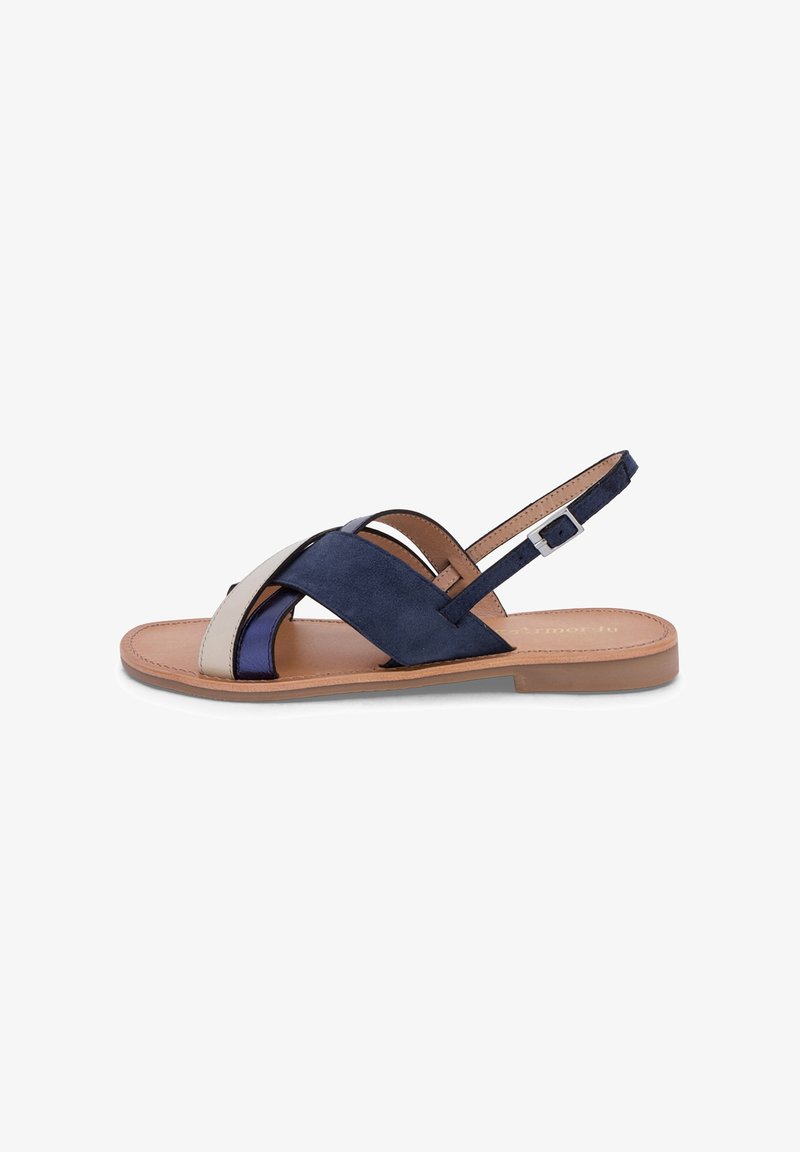Sandalia plana con suela marrón claro y tiras cruzadas en azul marino, azul oscuro y beige, con una correa ajustable con hebilla en el tobillo.