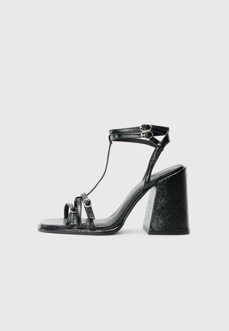 Black heeled sandals with a shiny patent finish, featuring multiple straps, circular hardware accents, and a chunky square heel.