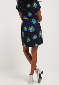 Vestido floral azul marino con flores turquesas y centros naranjas, de mangas cortas y silueta ajustada. Combinado con botas de tobillo plateadas.