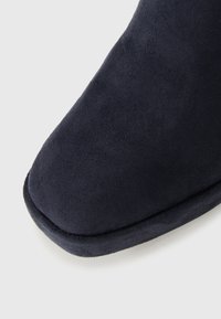 Gros plan de la partie avant d'une chaussure en suede bleu marine avec un bout carré arrondi et une couture visible le long de la semelle.