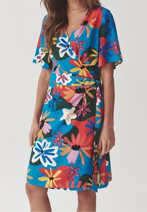 Woman wearing a knee-length wrap dress with short sleeves, featuring a colorful large floral pattern in blue, red, yellow, white, and pink.
