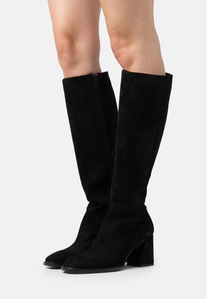 Bottes noires en daim montantes jusqu'au genou avec un bout carré, un talon bloc robuste et un zip sur le côté. Texture lisse et design ajusté.