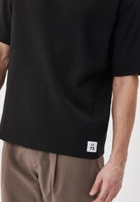Juoda trumpa rankovė t-shirt, pagaminta iš medvilnės, su paprastu dizainu ir baltu etiketu su tekstu "M 73" ant krašto.