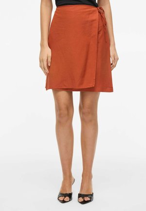 Rust-oransje omslagskjørt knyttet i midjen, brukt med svarte åpne tåhæl sko, vist fra midje til føtter mot hvit bakgrunn.