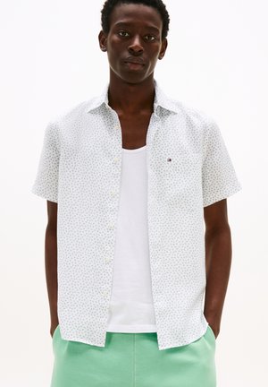 Chemise à manches courtes blanche avec un motif floral vert et bleu. Présente un col boutonné et une petite poche poitrine.