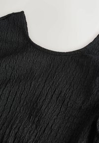 Haut en tissu noir texturé avec manches courtes et encolure arrondie, présenté à plat sur un fond clair.