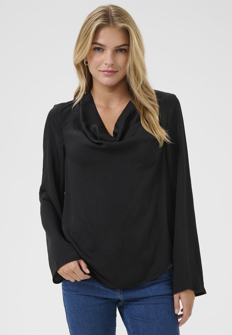 Sort bluse med cowl-neck og lange ærmer, lavet af blødt stof. Har en afslappet pasform og subtil struktur, parret med blå jeans.
