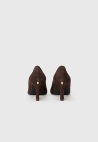 Brune semskede høydehæler med spiss tå og avsmalnet hæl, med en liten gullakent på baksiden. Glatt tekstur, minimalistisk design.