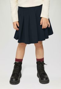 Marineblauwe geplooide rok met een elastische tailleband, gecombineerd met zwarte veterschoenen en bordeauxrode geribbelde sokken. Eenvoudig ontwerp met een soepele textuur.