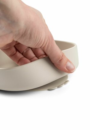 Ciotola in silicone beige chiaro con forma arrotondata, caratterizzata da una superficie liscia e una base piccola rimovibile per la stabilità. Mano posizionata sopra la ciotola.