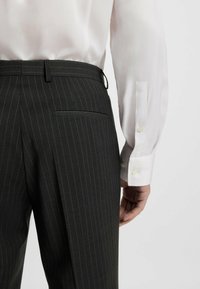 Schwarze taillierte Hose mit Nadelstreifen, waistband und Gesäßtasche. Kombiniert mit einem weißen Langarmhemd mit Knopfmanschetten.