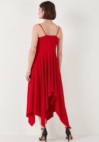 Rotes, ärmelloses Kleid mit einem taillierten Oberteil und einem schwingenden, asymmetrischen Saum. Der Stoff wirkt leicht mit einer glatten Textur.