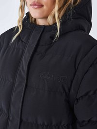 Sort puff jakke med høj krave og hætte. Har indsyede paneler, broderet logo og en glat, mat tekstur.