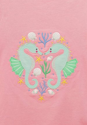 Zwei minzgrüne Seepferdchen, die sich gegenüberstehen, umgeben von Seesternen, Muscheln und Korallen, auf einem rosa Stoffhintergrund.