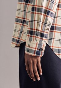 Camicia a quadri con bottoni nei colori beige, navy e ruggine; presenta una texture morbida, maniche lunghe e polsini con bottone.