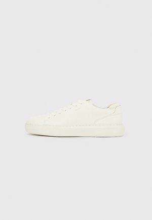 Bílá nízká teniska s přední šněrováním, hladkým koženým svrškem a tlustou gumovou podrážkou zobrazená z vnější strany na jednobarevném pozadí.