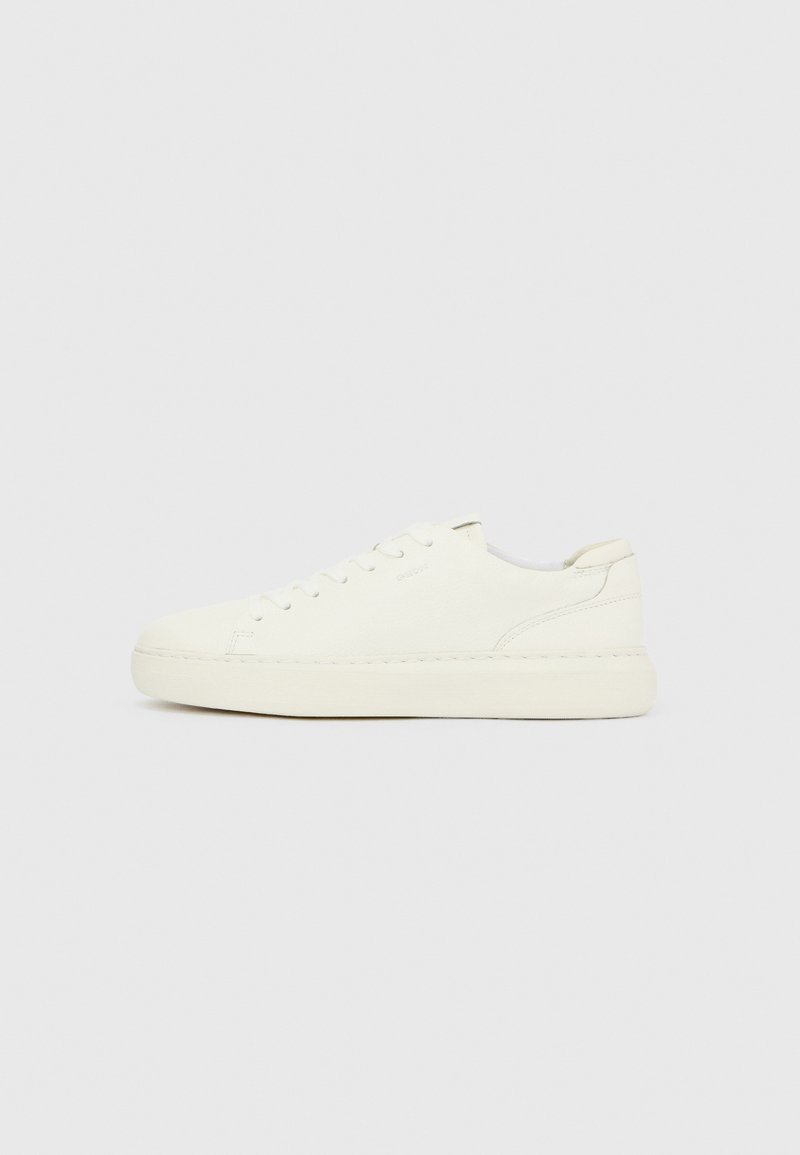 Baskets basses blanches avec laçage à l'avant, dessus en cuir lisse et semelle épaisse en caoutchouc, vues de côté extérieur sur un fond uni.