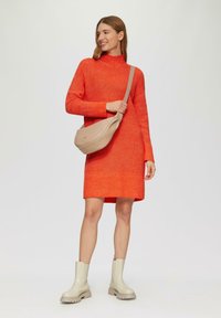 Helles orange gestricktes Kleid mit hohem Kragen und langen Ärmeln, kombiniert mit einer beigefarbenen Leder-Slingtasche und cremefarbenen Knöchelstiefeln mit dicken Sohlen.