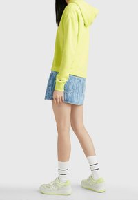 Neon gul hoodie med dragsko, i kombination med en ljusblå denim mini kjol. Utrustad med vita sneakers och randiga korta strumpor.