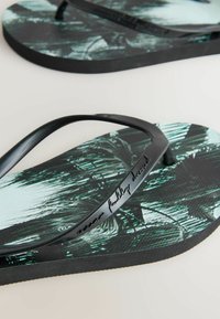 Sorte flip-flops med en tekstureret sål, prydet med et palmebladmønster i nuancer af grøn og sort, samt en buet rem med præget tekst.