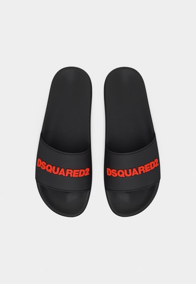 Μαύρα σανδάλια με σαγιονάρες με το κόκκινο λογότυπο «DSQUARED2» στις φαρδιές τιράντες, τοποθετημένα δίπλα δίπλα σε ανοιχτό φόντο.