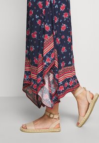 Robe bleu marine avec motif floral rouge et ourlet rayé ; associée à des sandales espadrilles beige clair à bride avec boucle.