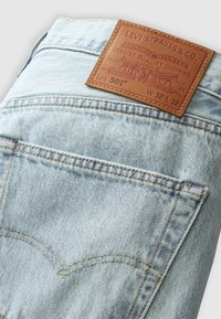 Jeans in denim azzurro chiaro con una patch in pelle etichettata "LEVI STRAUSS & CO." sopra la tasca posteriore, che mostra un design e cuciture classiche.