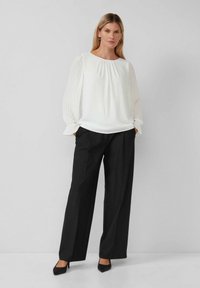Witte blouse met lange mouwen en geplooide mouwen, gecombineerd met zwarte wijde broek en zwarte hoge hakken.