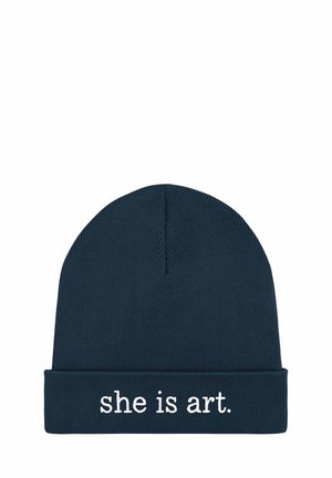 Marineblauwe gebreide muts met opgerolde boord en witte geborduurde tekst "she is art." gecentreerd op de voorkant.