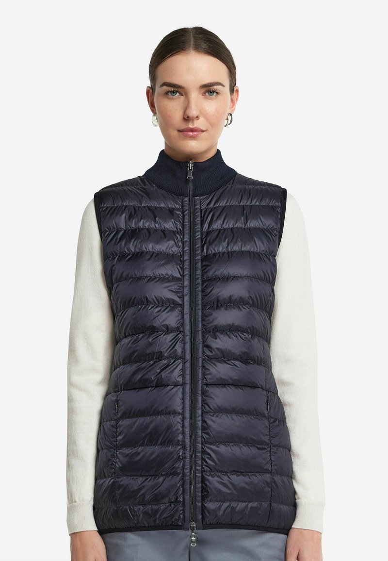 Marinblå pufferväst med horisontell quiltad design, hög krage och framdragkedja. Har en slät, glänsande yta och två fickor.