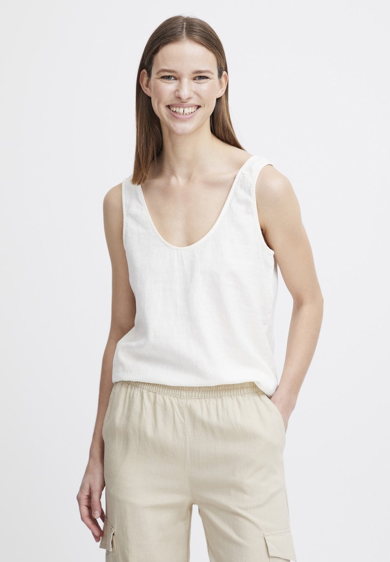 Weißes Leinen-Tanktop mit einem Rundhalsausschnitt und breiten Trägern, kombiniert mit beigen Hochgezogen-Hosen mit elastischem Bund, die Taschen und eine weiche Textur besitzen.