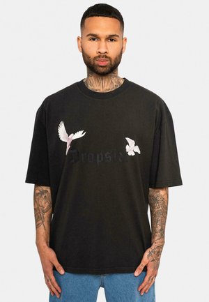 Svart oversized t-skjorte med hvite og rosa fuglemønstre på forsiden, har rund hals og kortermet, laget av bomullsmateriale.