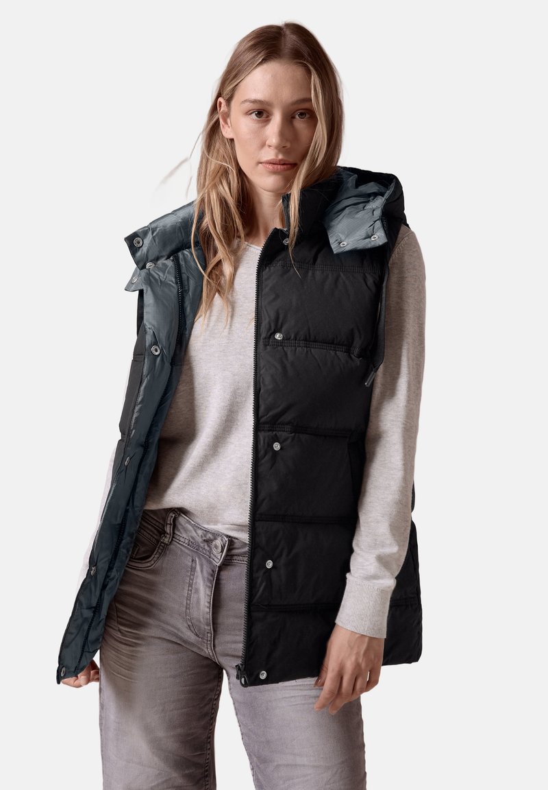 Schwarze Steppweste mit abnehmbarer türkisfarbener Kapuze, ausgestattet mit Druckknöpfen, Reißverschluss und seitlichen Taschen. Tragen über einem hellgrauen Oberteil.