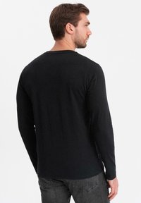 Zwarte langharige shirt, gemaakt van zacht katoen, ronde halslijn, getailleerd ontwerp, eenvoudig zonder patronen, weergegeven vanuit de achterkant.