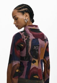 Cămașă din material cu model, cu imprimeu îndrăzneț și colorat cu buze; design cu guler, mâneci lungi și culoare de bază neagră.